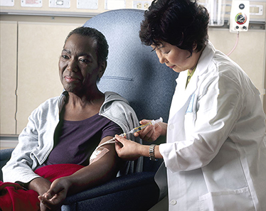 An Asian female nurse administers chemotherapy to an African-American woman through a catheter in her left arm.