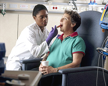 An African-American female nurse administers oral chemotherapy to an older Caucasian female patient in a clinical setting.